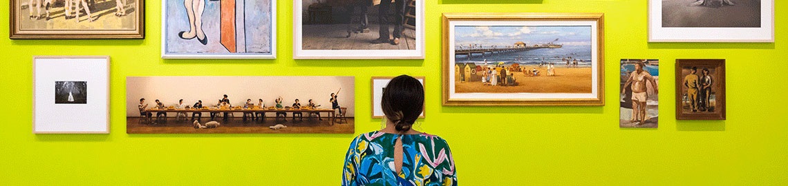 Woman standing in front of different paintings arranged on a wall
